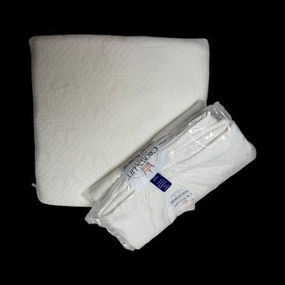 A white quilted mattress topper or comforter shown next to a packaged stack of matching folded white sheets on a solid black background. The packaging label reads 'Comfort Lift'try it experience comes with pocket pillowcase and choice of ONE core insert for $45 plus $6.90 shipping